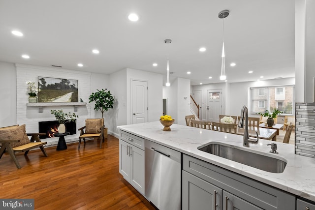 kitchen featuring light stone countertops, dark wood-style flooring, gray cabinetry, a sink, and dishwasher