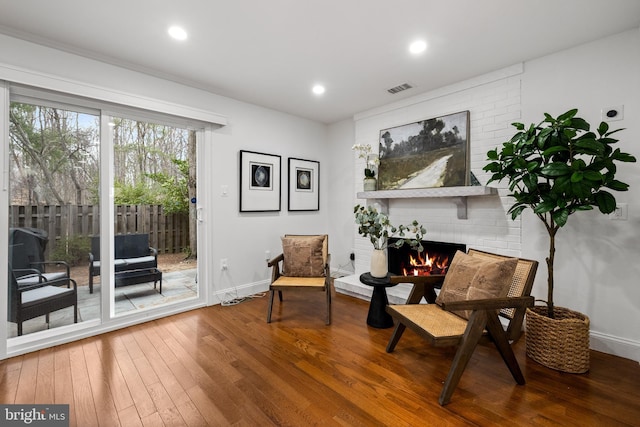 living area with visible vents, hardwood / wood-style flooring, recessed lighting, baseboards, and a brick fireplace