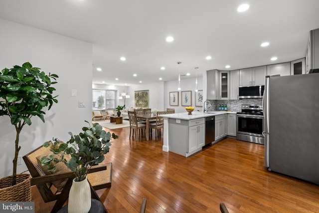 kitchen with gray cabinets, stainless steel appliances, a peninsula, glass insert cabinets, and dark wood-style flooring