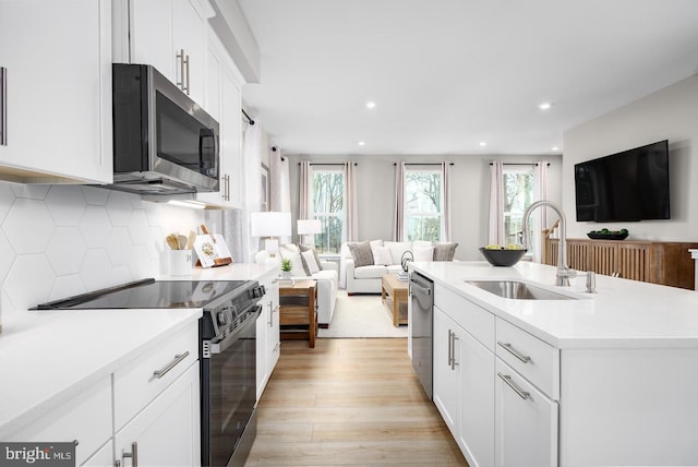 kitchen with stainless steel appliances, a sink, open floor plan, light countertops, and a center island with sink