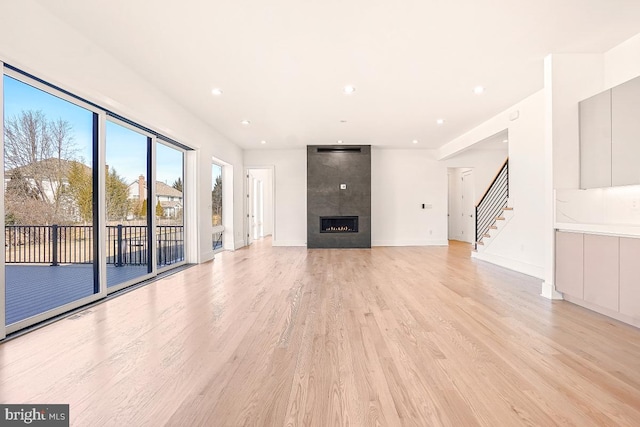 unfurnished living room with recessed lighting, a large fireplace, baseboards, stairway, and light wood-type flooring