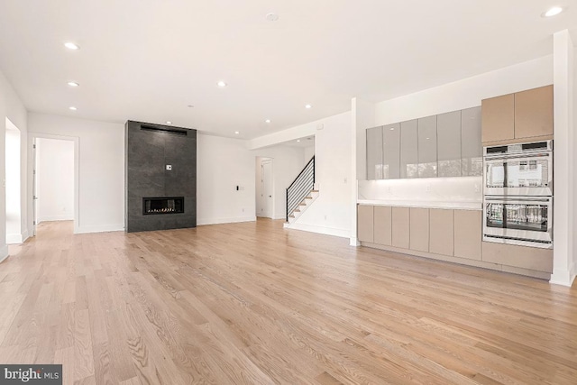 unfurnished living room with light wood finished floors, baseboards, a tile fireplace, stairway, and recessed lighting