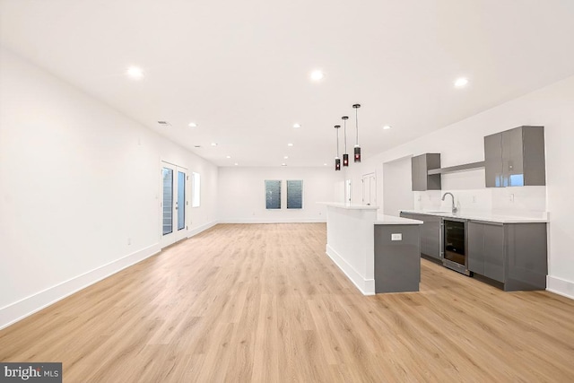 kitchen featuring light wood-style flooring, gray cabinetry, beverage cooler, a sink, and light countertops