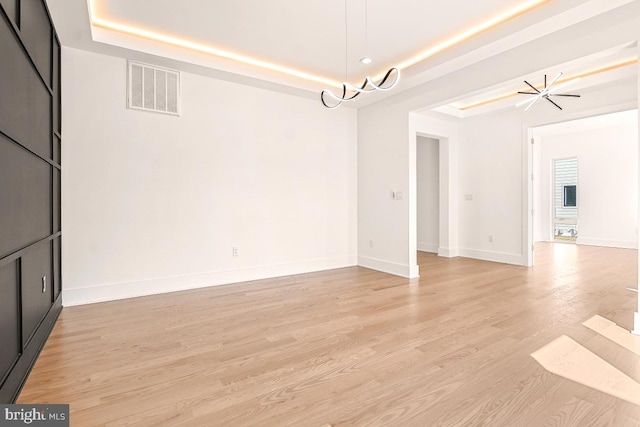 unfurnished dining area featuring light wood-style flooring, a raised ceiling, visible vents, and baseboards