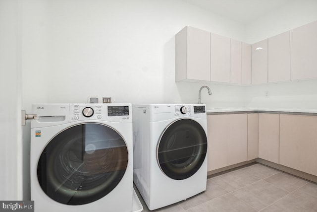 laundry area featuring cabinet space, light tile patterned floors, washer and clothes dryer, and a sink