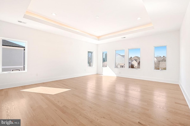 unfurnished living room with light wood-style flooring, a raised ceiling, and visible vents