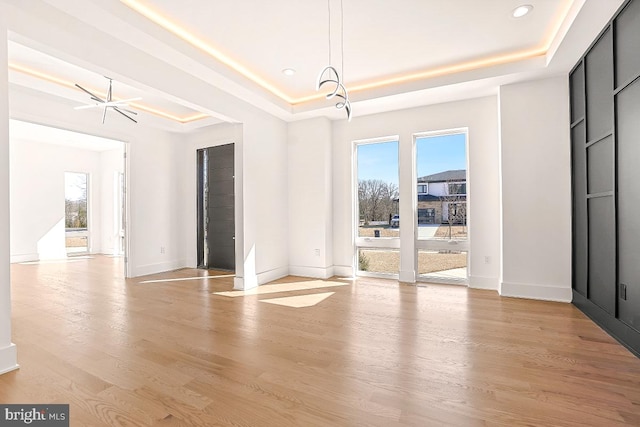 interior space featuring light wood-type flooring, a raised ceiling, and baseboards