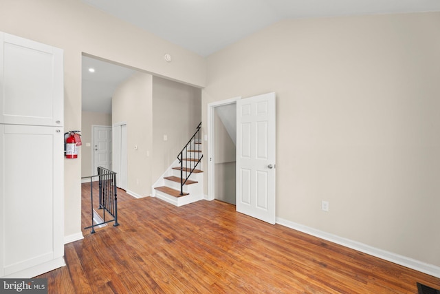 spare room featuring lofted ceiling, visible vents, stairway, wood finished floors, and baseboards