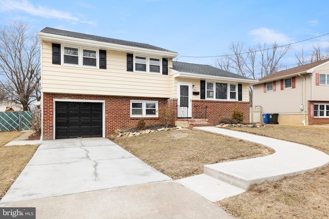 tri-level home featuring an attached garage, fence, concrete driveway, and brick siding