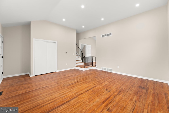 interior space with vaulted ceiling, stairway, wood finished floors, and visible vents