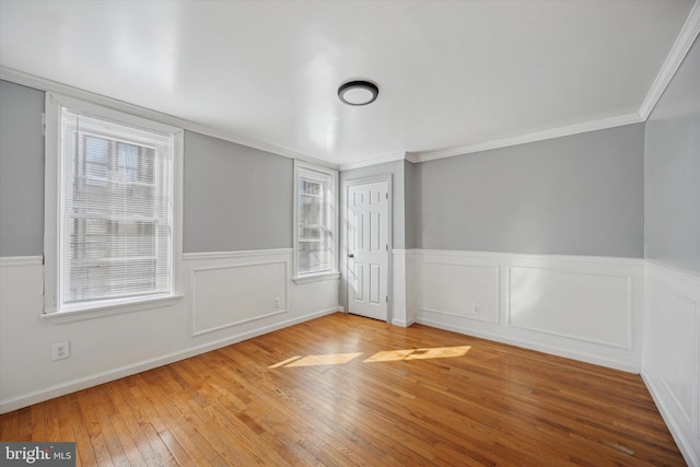 empty room with a wainscoted wall, ornamental molding, and wood finished floors