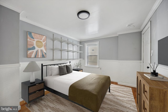 bedroom featuring light wood-style floors, ornamental molding, and wainscoting