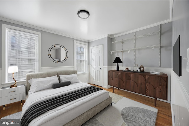 bedroom with a wainscoted wall, ornamental molding, a closet, and wood finished floors