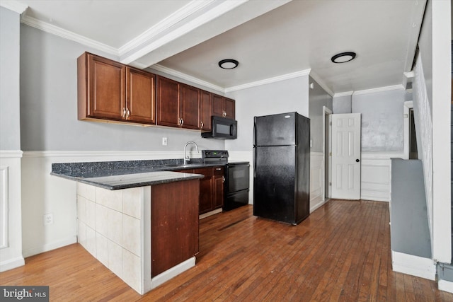 kitchen featuring dark stone counters, a sink, ornamental molding, dark wood-style floors, and black appliances