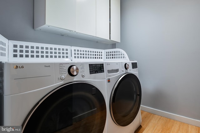 laundry area featuring light wood-type flooring, independent washer and dryer, cabinet space, and baseboards