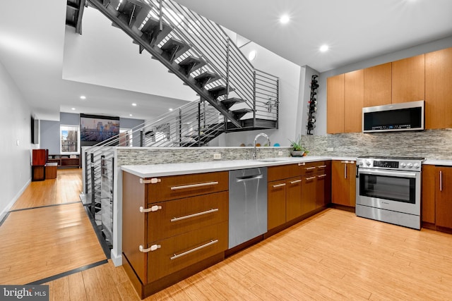 kitchen with decorative backsplash, appliances with stainless steel finishes, a peninsula, light wood-style floors, and a sink