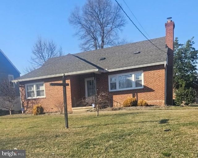 view of front of house featuring a shingled roof, a front yard, brick siding, and a chimney