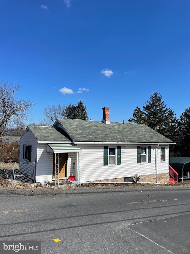 view of front of home with a shingled roof, fence, and a chimney