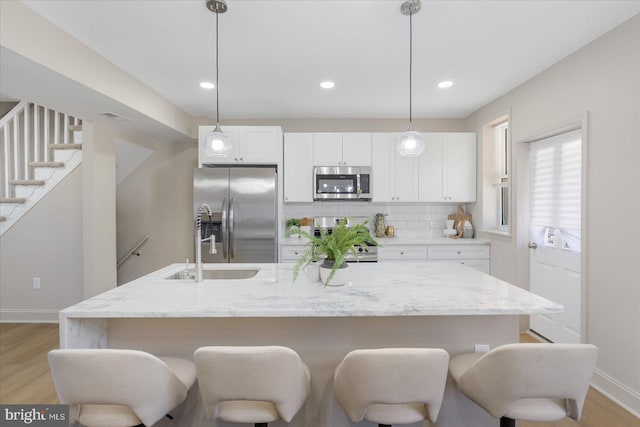 kitchen featuring a breakfast bar, stainless steel appliances, light wood-style floors, white cabinets, and decorative backsplash