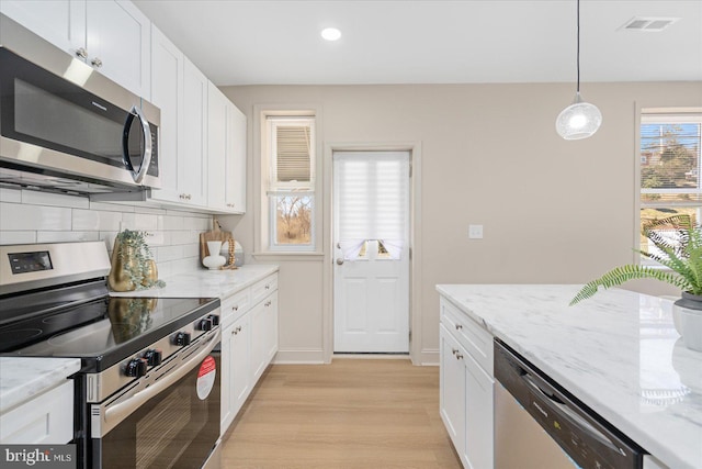 kitchen with backsplash, light wood-style floors, appliances with stainless steel finishes, white cabinets, and light stone countertops