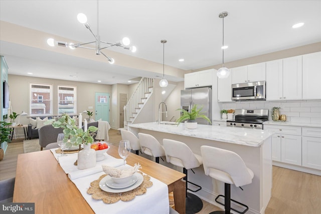 kitchen with light wood finished floors, backsplash, appliances with stainless steel finishes, and white cabinetry