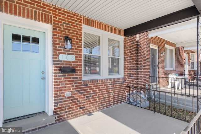 view of exterior entry featuring brick siding and a porch