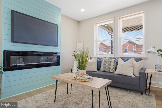 living room featuring a glass covered fireplace, recessed lighting, baseboards, and wood finished floors