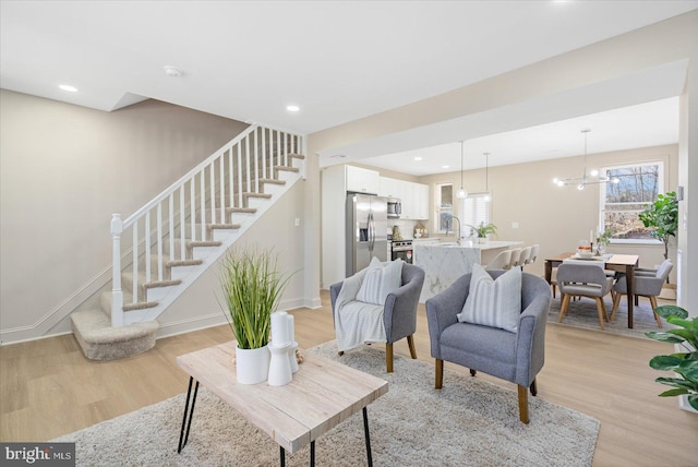 living area with baseboards, light wood-style flooring, recessed lighting, stairs, and a chandelier