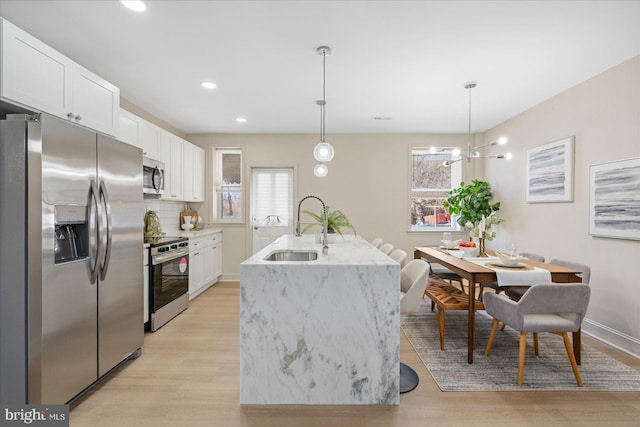 kitchen with light wood-style flooring, a sink, white cabinetry, stainless steel appliances, and light stone countertops