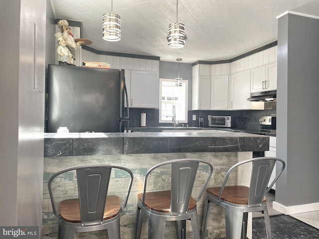 kitchen with freestanding refrigerator, a sink, under cabinet range hood, white cabinetry, and backsplash