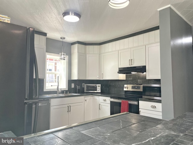 kitchen featuring tasteful backsplash, dark countertops, under cabinet range hood, appliances with stainless steel finishes, and a sink