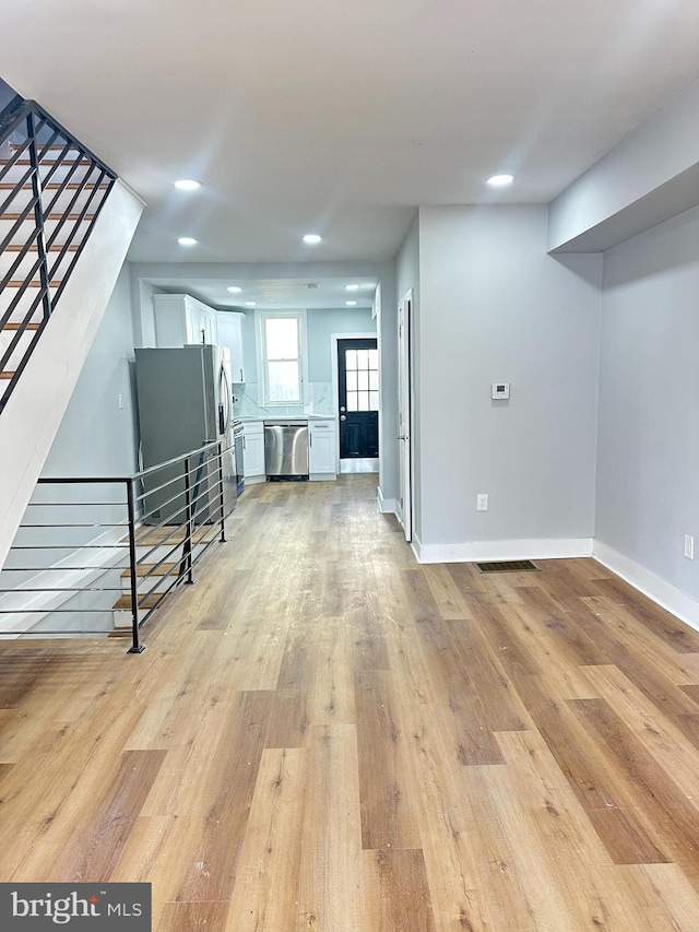 unfurnished living room with light wood-type flooring, stairway, baseboards, and recessed lighting