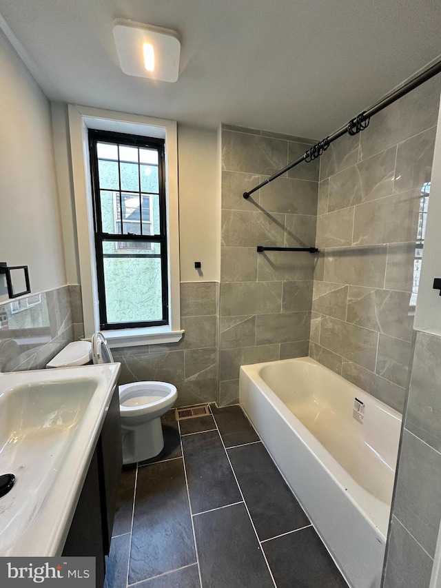 full bathroom featuring toilet, a sink, tile walls, shower / washtub combination, and wainscoting