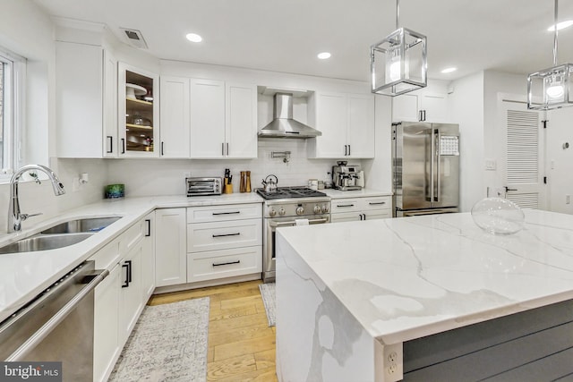 kitchen featuring pendant lighting, glass insert cabinets, a sink, wall chimney range hood, and high quality appliances