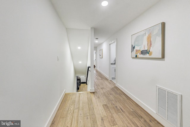hall featuring light wood finished floors, baseboards, visible vents, and an upstairs landing