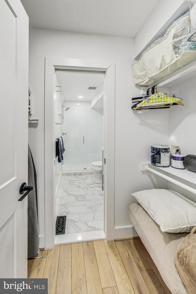interior space with toilet, a stall shower, visible vents, and wood finished floors