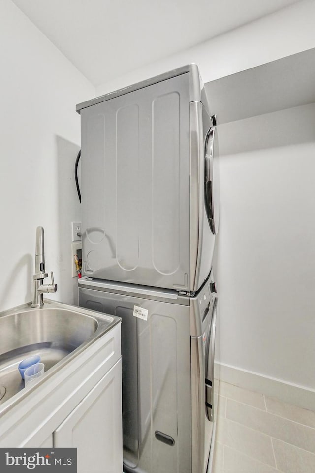 clothes washing area featuring light tile patterned floors, cabinet space, a sink, stacked washing maching and dryer, and baseboards