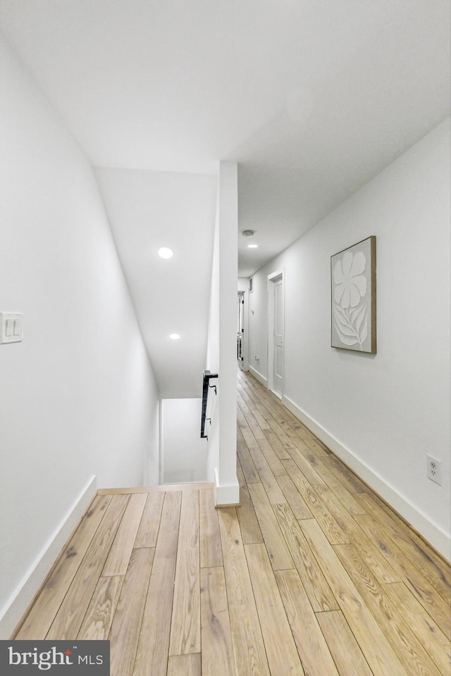 corridor with baseboards, an upstairs landing, and light wood-style floors