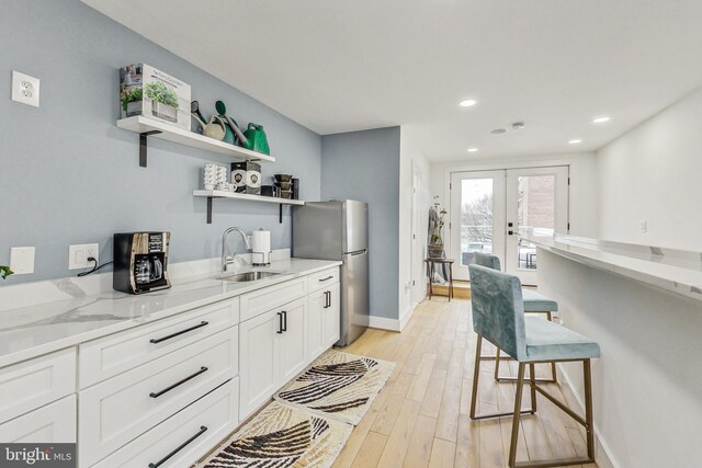 kitchen with light stone counters, french doors, open shelves, white cabinets, and a sink