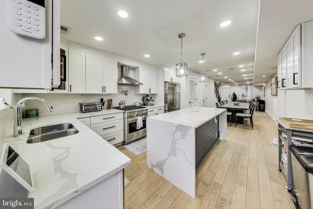 kitchen featuring light stone counters, white cabinets, wall chimney range hood, a center island, and high end appliances