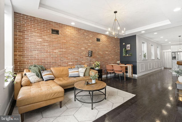 living room featuring brick wall, an accent wall, wood finished floors, a tray ceiling, and a chandelier