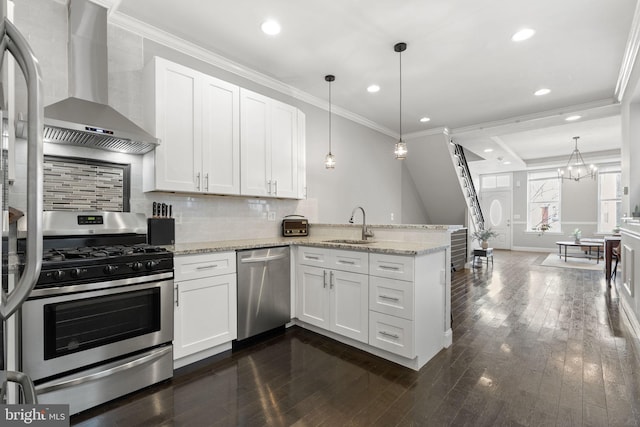 kitchen with a peninsula, stainless steel appliances, a sink, white cabinetry, and wall chimney exhaust hood