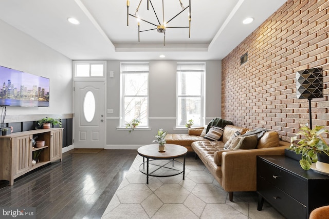 living room featuring baseboards, a raised ceiling, brick wall, an accent wall, and wood finished floors