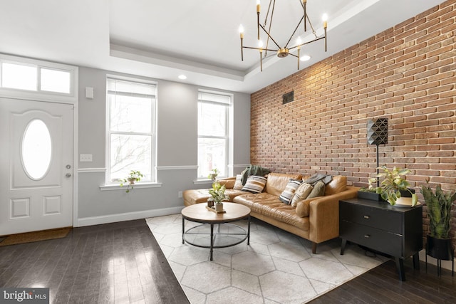 living room with an accent wall, brick wall, hardwood / wood-style floors, baseboards, and a tray ceiling