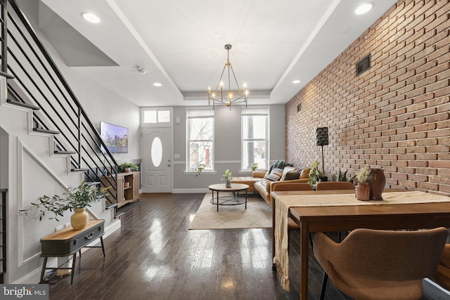 entryway featuring brick wall, an accent wall, stairway, dark wood-type flooring, and a tray ceiling