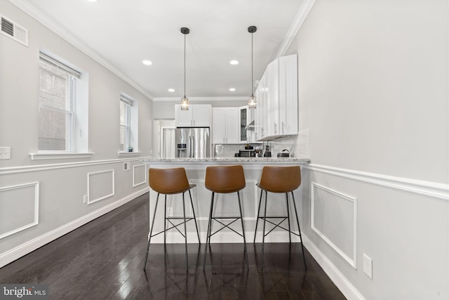 kitchen featuring a decorative wall, stainless steel fridge, visible vents, and white cabinets