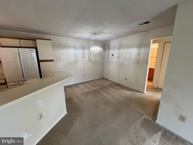 unfurnished dining area featuring baseboards, visible vents, light colored carpet, a textured ceiling, and a chandelier