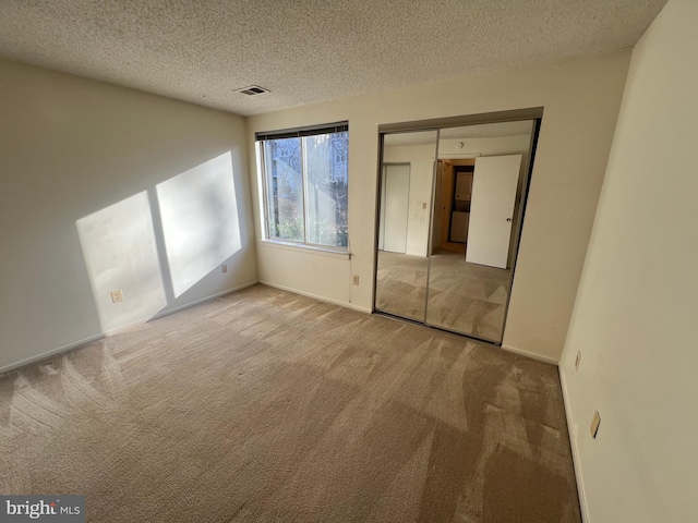 unfurnished bedroom with light colored carpet, visible vents, and a textured ceiling