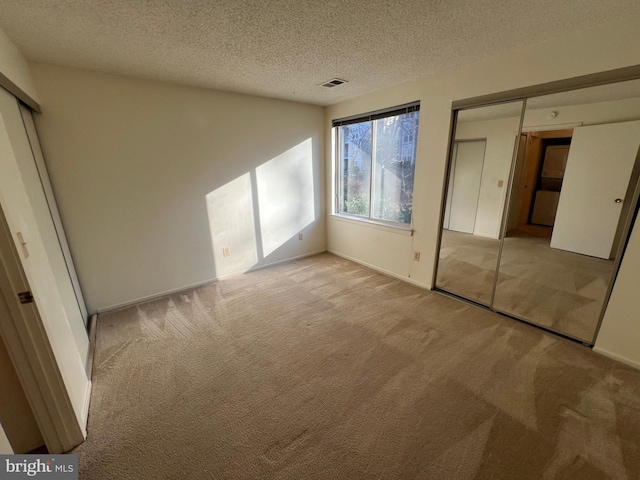 unfurnished bedroom with light colored carpet, visible vents, and a textured ceiling