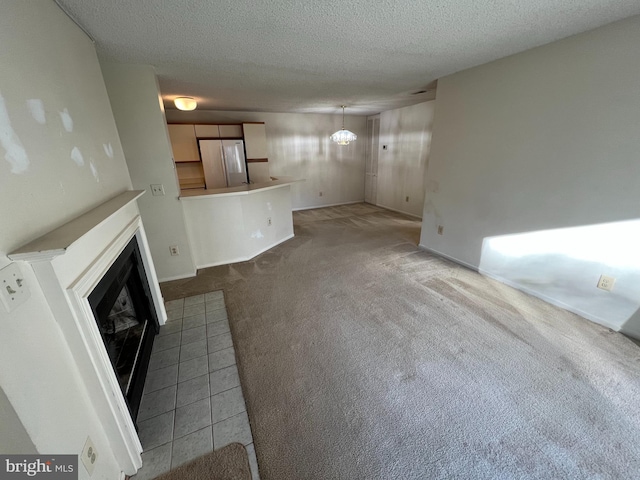 unfurnished living room featuring an inviting chandelier, a fireplace with flush hearth, a textured ceiling, and light colored carpet